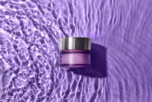 Luxury skincare cream jar floating on rippling purple water surface