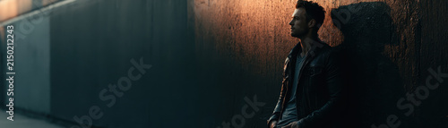 Man wall urban shadow moody fashion street leather jacket cool Stylish man leaning urban wall shadowy moody light fashion street leather jacket cool attitude confident pose city evening atmosphere