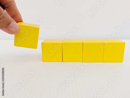 yellow building blocks. Hand holding a yellow cube block to arrange in line on the white table