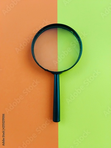 A magnifying glass isolated on a green and orange coloured background. Concept photography