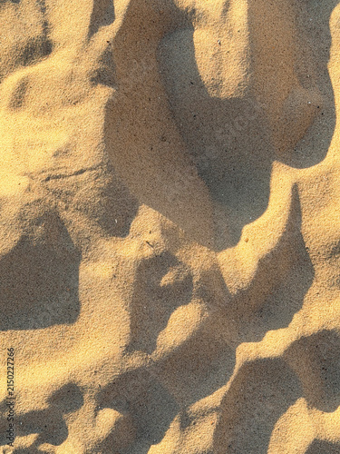 Close-up beach sand during golden hour.  The shadows accentuate the sand's natural contours, enhancing the depth and detail of the surface. The overall effect is a warm and serene scene