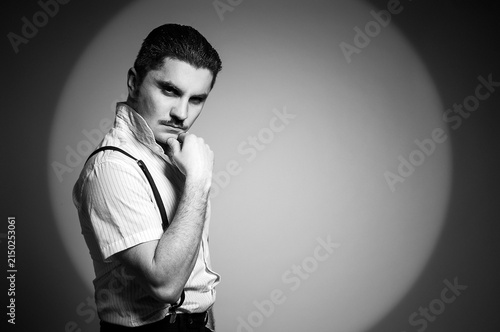 Man in white shirt with fancy mustache standing on a stage illuminated by the spotlight