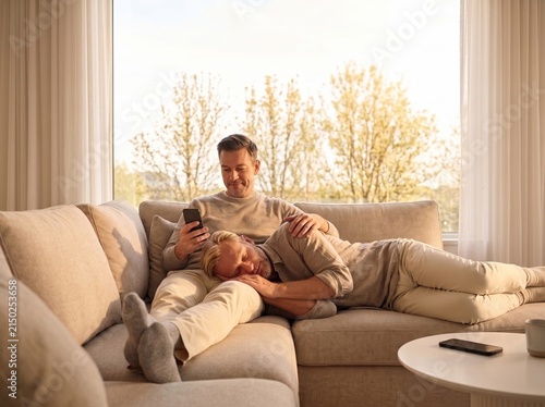 Two Men Relaxing Together on a Cozy Sofa at Home, Warm Lifestyle and Relationship Concept. Copy space