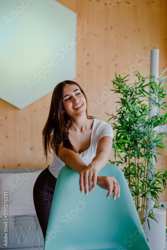Quadro su tela Happy young woman laughing naturally while leaning over a turquoise chair in a b