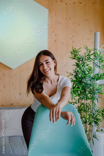 Fotografía Happy young woman laughing naturally while leaning over a turquoise chair in a b