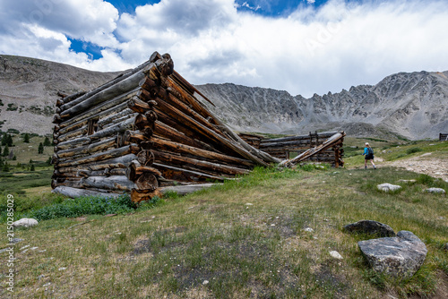 Woman hiker exploring abandoned mining cabins on Mayflower Gulch trail near Copper Mountain, Colorado under summer afternoon cloudscape.