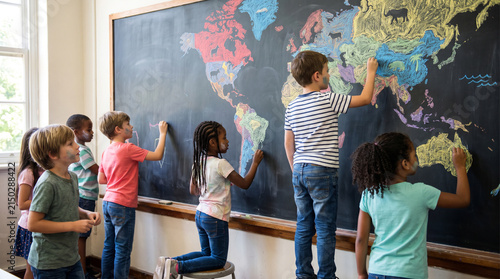 Diverse group of happy school children drawing a colorful world map on a black chalkboard in class