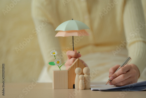 Home insurance concept, woman holding umbrella over miniature house and flowers for property protection, home insurance, safety, coverage, security, protection