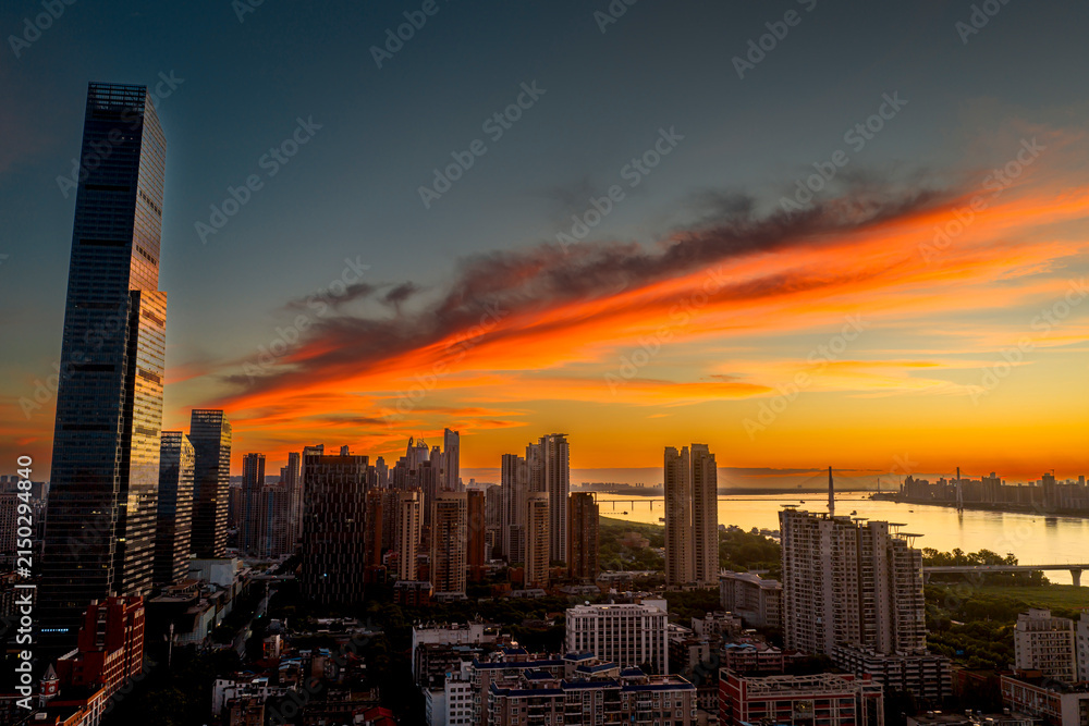 Fototapeta premium Wuhan CBD skyline illuminated by a dramatic fiery sunrise. These brilliant burning clouds above towering skyscrapers symbolize a blazing, prosperous economy and the dawn of a dynamic financial future