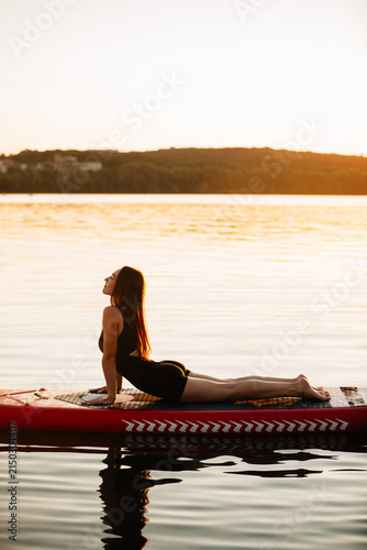 Woman practicing sup yoga at sunset on water
