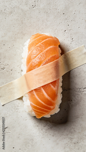 Sushi on light concrete background. Salmon nigiri duct-taped to a wall. Creative, modern, food art, safe packaging design concept. Japanese, oriental fusion restaurant menu, Vertical, close up