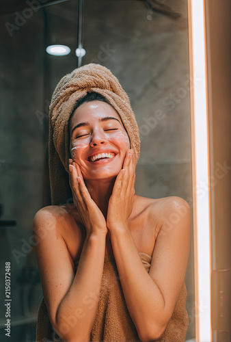 Young Woman Applying Face Cream with Towel on Head Smiling Happily.