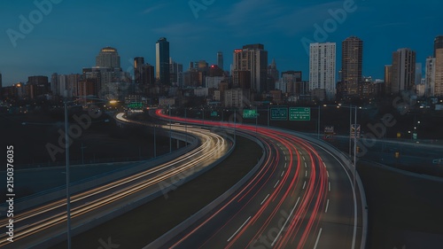 Dynamic city highway at night, long exposure captures vibrant light trails from moving vehicles, urban skyline.