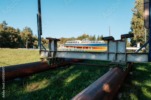 Quadro su tela Old passenger boat in dry dock viewed through metal rails and industrial structures on a sunny day