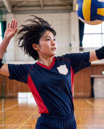 体育館でバレーボールのスパイクを打つ真剣な表情の若い女性