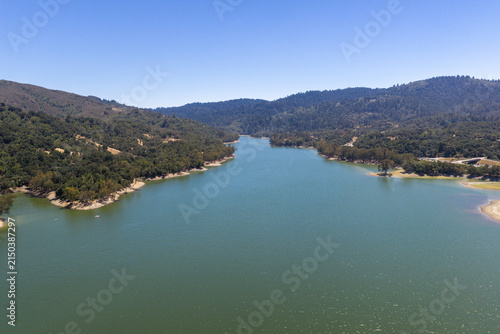 Lexington Reservoir water level appearing low against hills and trees under a clear blue sky, illustrating environmental concerns and water resource management in California