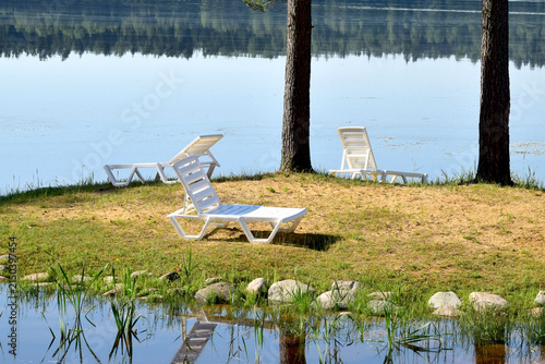 Summer landscape. Empty deck chairs stand on the shore of a forest lake.