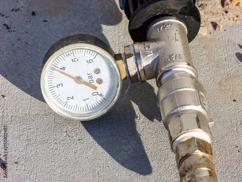 Pressure gauge on a metal pipe displays about 3 bar on the concrete, close-up showing system control.