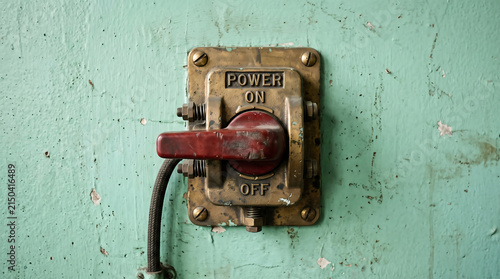 Vintage industrial mechanical toggle switch with brass plate and red lever on grungy green wall
