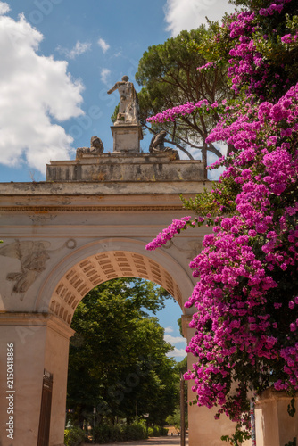 Arco Romano in the Villa Borghese Park in Rome, Italy a summer day with blue sky. Pink flowering trees