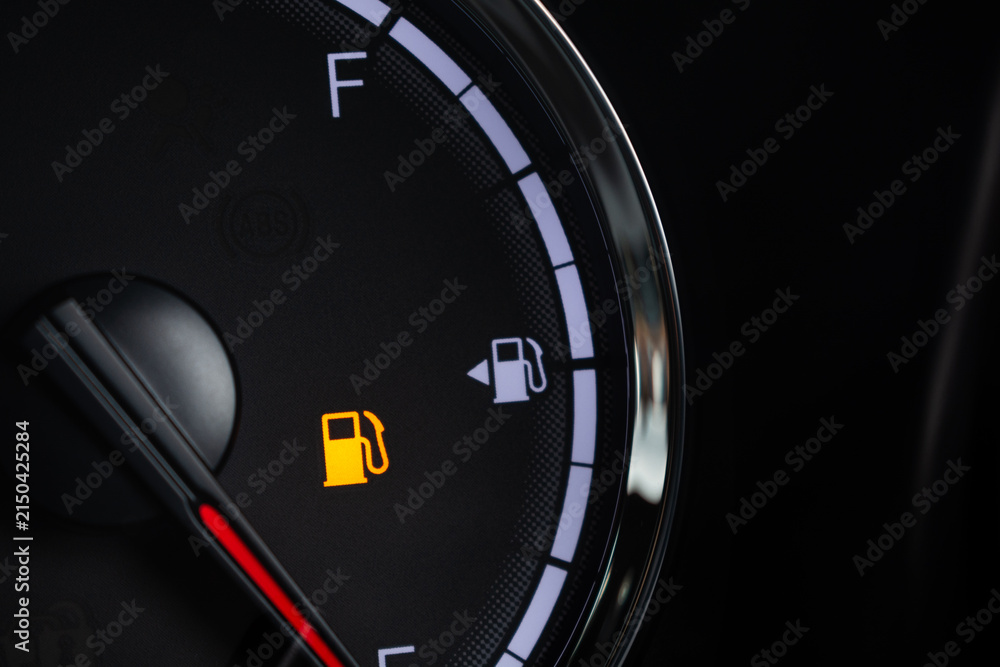 Naklejka premium Fuel gauge with warning indicating low fuel tank on car dashboard