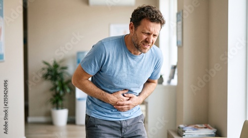 Middle-aged man suffering from acute abdominal pain and stomach ache while standing indoors
