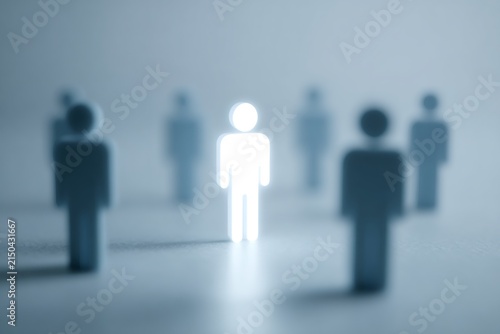 Glowing white human figure standing out among dark silhouettes. Innovation and leadership concept