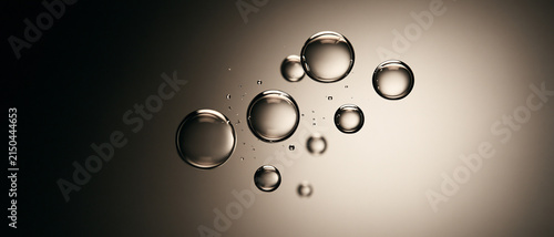 Transparent oil serum air bubbles floating on warm beige gradient background