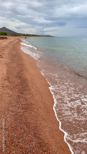 Empty beach with reddish pebbly sand and gentle shore break, overcast day vertival photo