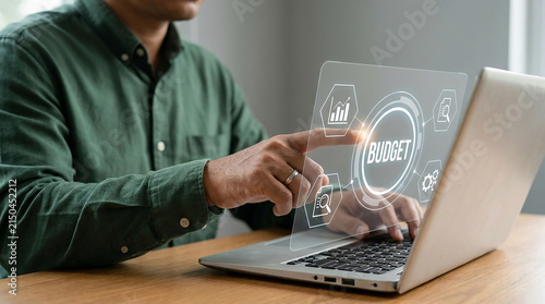 Budget Management on Laptop: A person uses a laptop to manage their budget, interacting with a futuristic holographic interface displaying financial icons and charts, indicating planning and analysis.