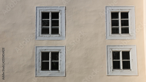four symmetrical white-framed windows on a cream plaster wall,