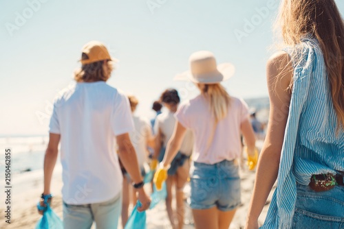 wide beach cleanup scene on a sunny summer day, volunteers shown from behind at medium distance, faces not visible
