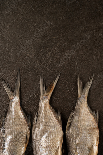 Photography Close up of three dried salted vobla fish tails lined up on dark brown textured surface with copy space