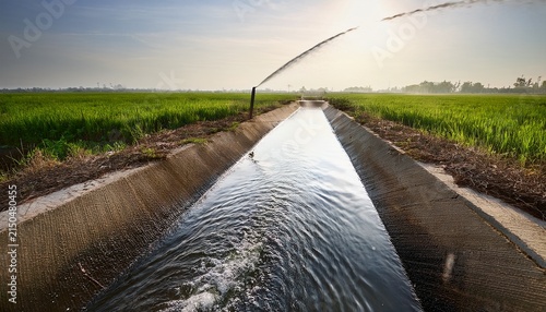 metal pipe discharging water into irrigation canal for crop field watering with concrete