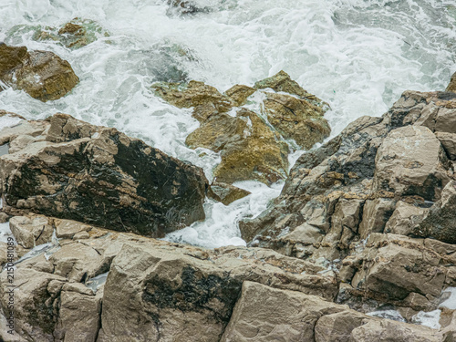Canvas Print Churning Sea Water and White Foam Splashing over Wet Coastal Rocks