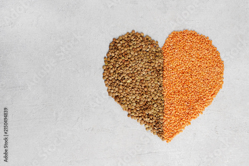 Heart shape made of brown and red lentils on gray background with copy space. Horizontal top view.