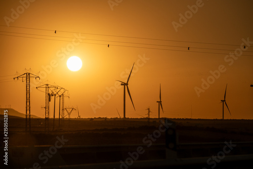 Fotografie Wind Farm and Power Lines Silhouetted Against Sunset Sky