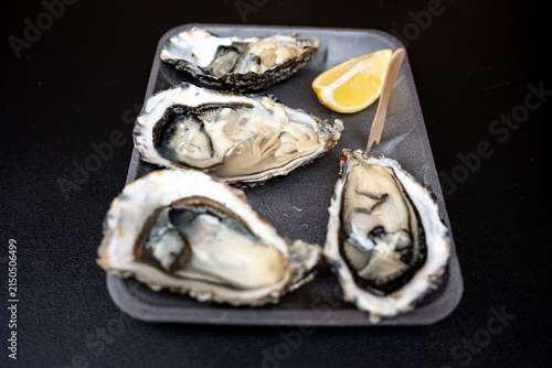 Fresh opened oysters on a black tray served with a slice of lemon and a wooden toothpick on a dark background.