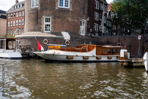 Luxury classic salon boat with a wooden steering wheel moored near a historic brick building in Amsterdam, Netherlands.