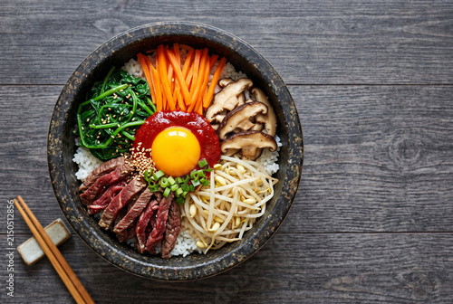 Top view of Korean bibimbap with raw beef and fresh ingredients in stone bowl