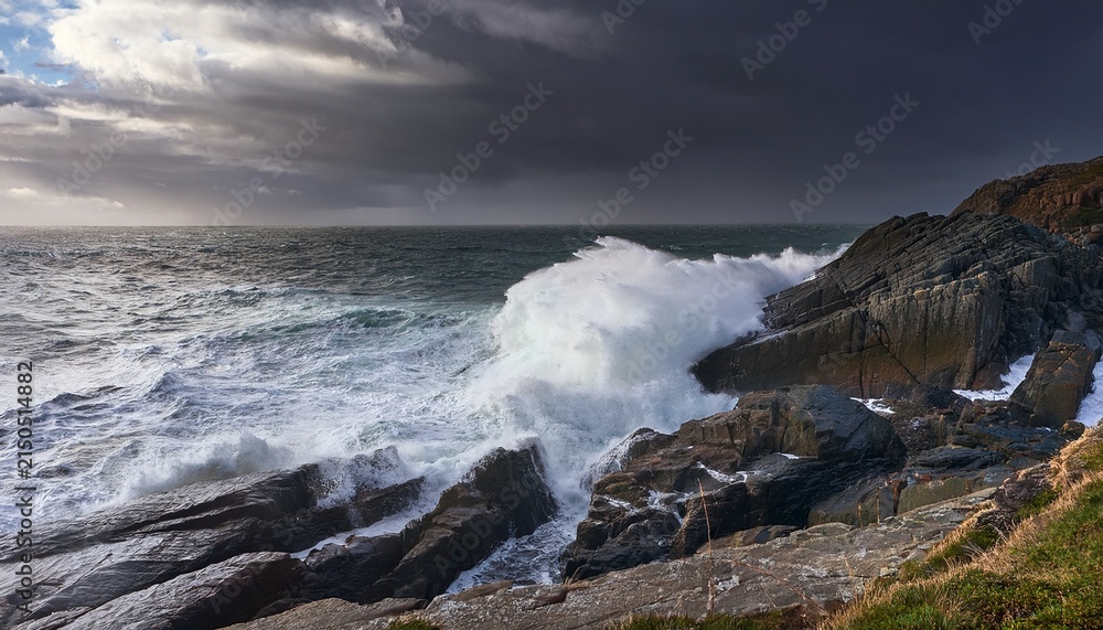Fototapeta premium A Rocky Coastline With A Large Wave Crashing Against The Shore Under A Stormy Sky