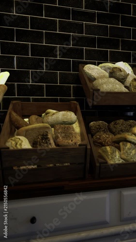 Loaves of bread sit invitingly in wooden crates. Baguettes lean gracefully, their golden crusts glowing against a sleek black tile background. The aroma of freshly baked bread fills the air.