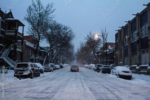American Residential street in Le Plateau, Montreal, Quebec, Canada, at winter dusk, with parked cars, snow-covered road, duplex houses, streetlights and a quiet neighborhood real estate setting.