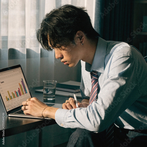 Successful and young and formal wear working with laptop while sitting in his office in front of computer screens with trading charts