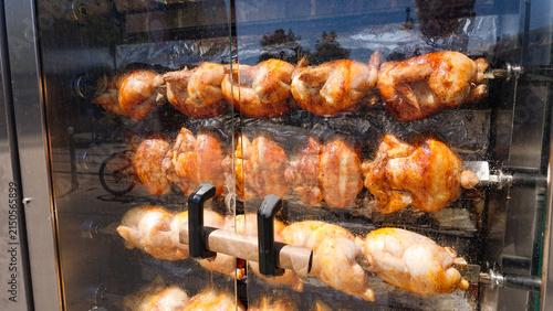 Foto Golden brown chickens cooking slowly on spits inside a rotisserie oven