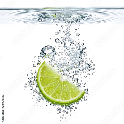 Fresh green lime slice falling through water with air bubbles on white background