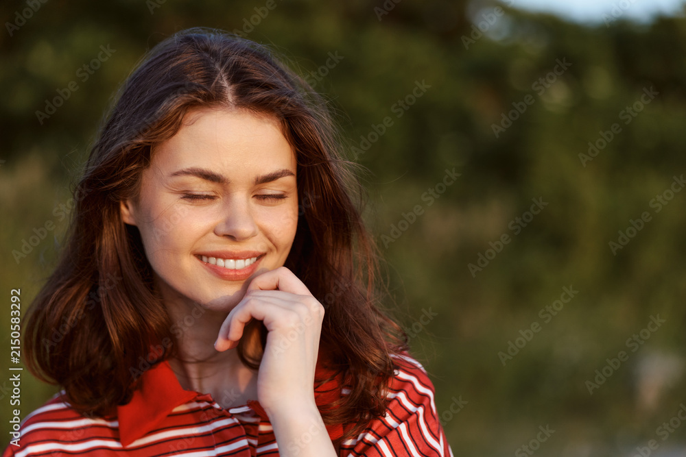 Obraz premium A smiling young woman enjoying nature in a portrait shot. The happy woman reflects a peaceful lifestyle outdoors during a sunny summer day. Concept for wellness, relaxation, and mindfulness.
