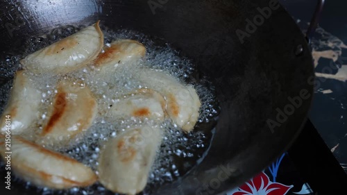 Dumplings frying in hot oil in a black wok, with bubbles and golden brown edges during cooking