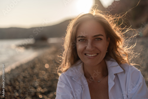 Woman beach sunset. Smiling young woman enjoying golden hour on a pebble beach, radiating natural beauty and happiness