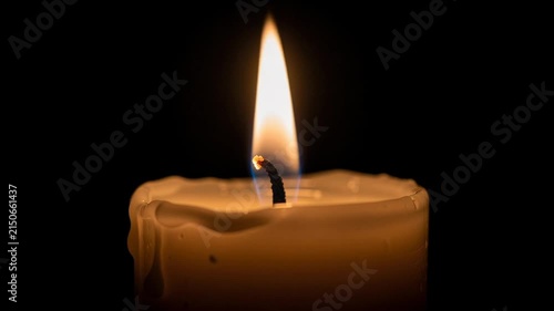 Close up of a melting candle flame glowing brightly in the dark with soft melted wax